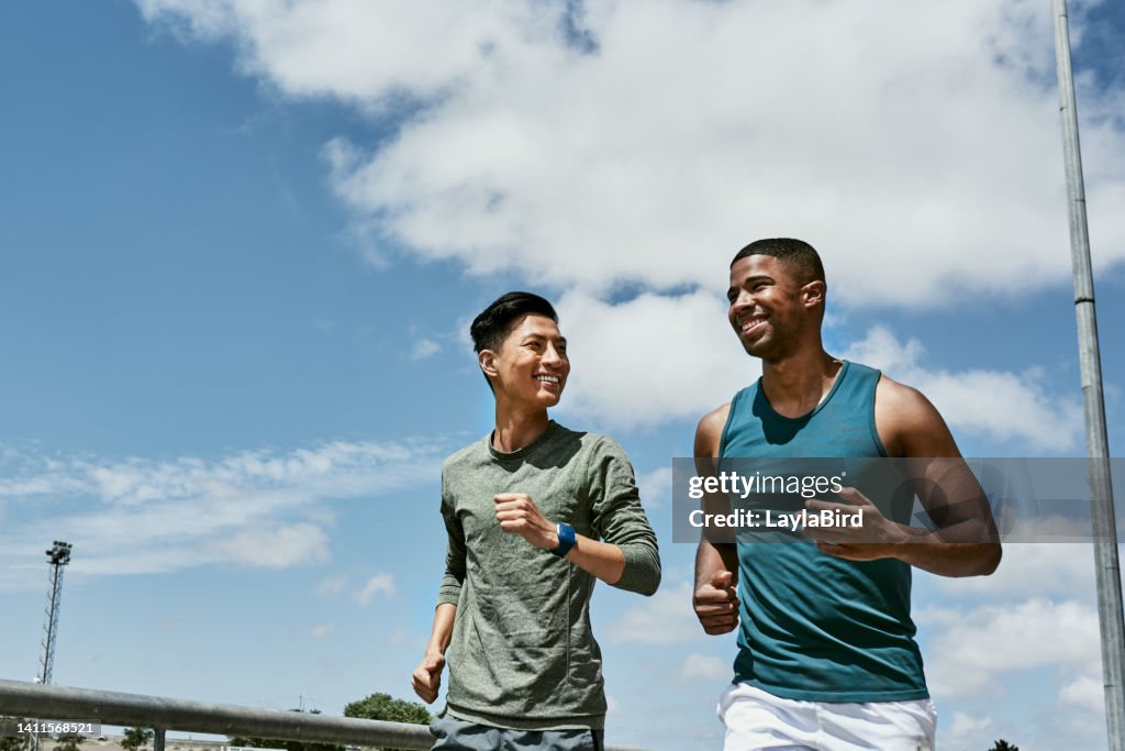 Active men jogging outdoors on blue cloudy sky with copy space. Two athletic guys or young sports friends running together, doing their routine cardio workout and fitness exercise in the city