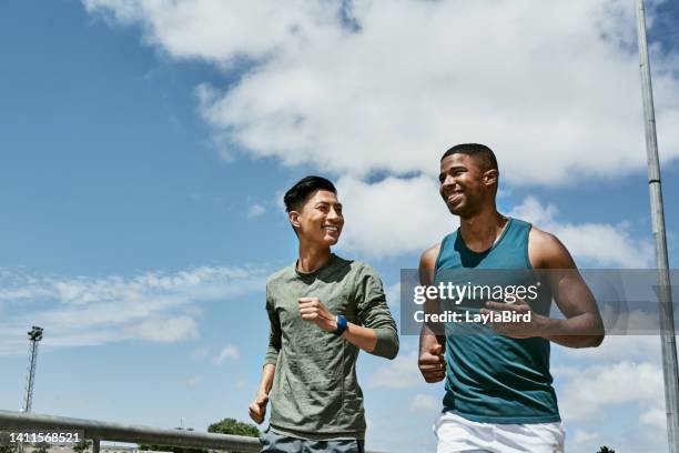 active men jogging outdoors on blue cloudy sky with copy space. two athletic guys or young sports friends running together, doing their routine cardio workout and fitness exercise in the city - men's health stock pictures, royalty-free photos & images