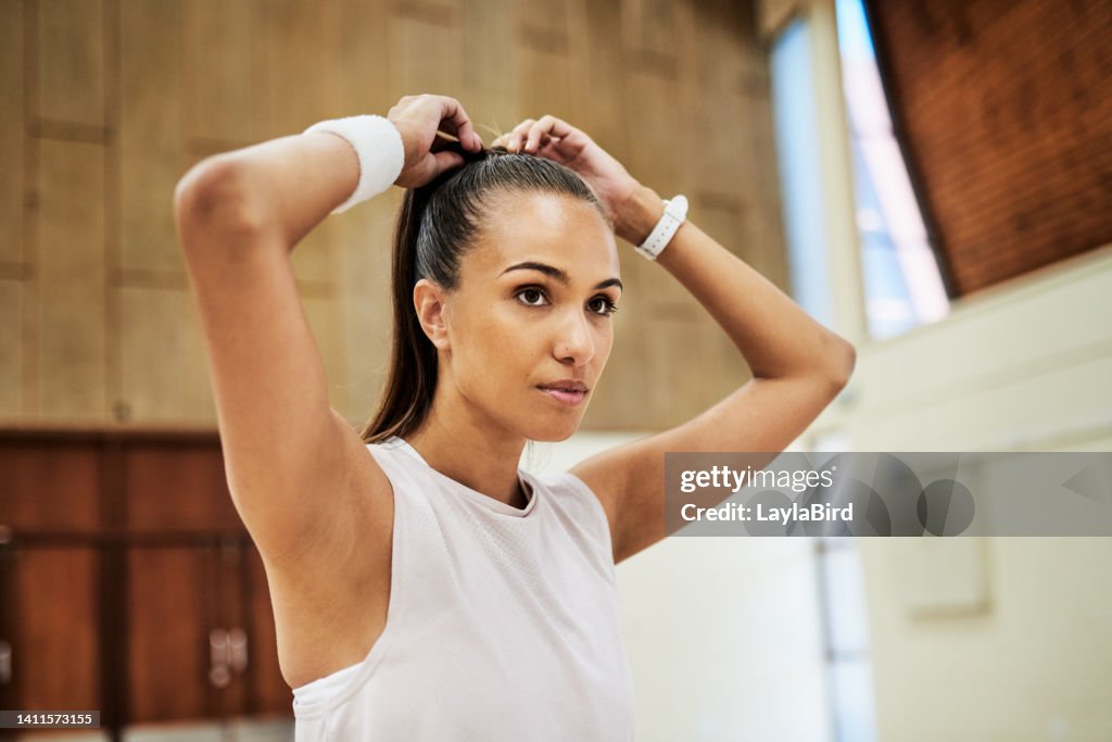 Fit young woman tying her hair while getting ready for exercising and training in a sport center or gym. One determined and dedicated athlete looking focused and prepared for a workout or competition