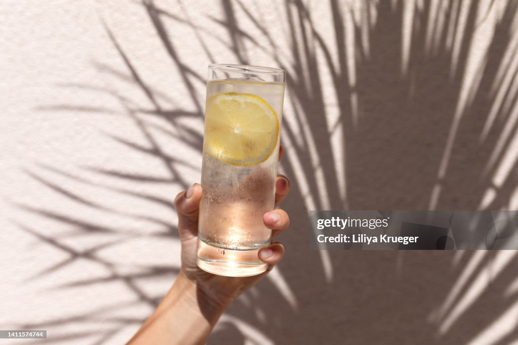 Glass of water with lemon in women's hand.