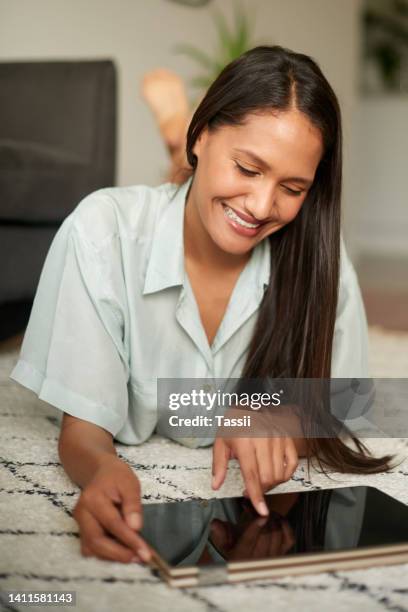 a young woman relaxing and watching videos on a tablet while lying on the floor at home. female watching video on a digital device resting in her house on a weekend. lady enjoying some entertainment - free download photo stock pictures, royalty-free photos & images