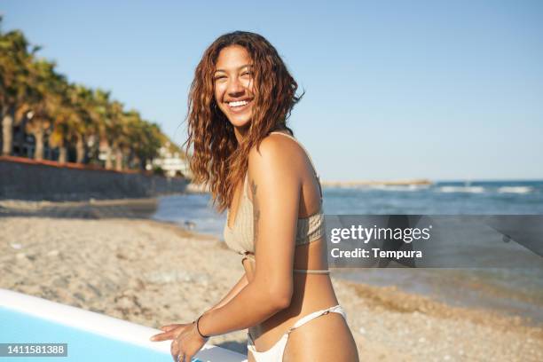 a woman stand is standing next to a paddle surfboard. - jamaicaanse etniciteit stockfoto's en -beelden