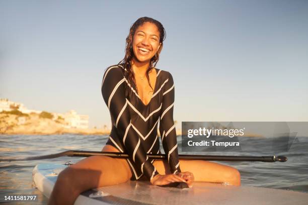 a woman is sitting and relaxing on a paddle surf boar. - jamaicaanse etniciteit stockfoto's en -beelden