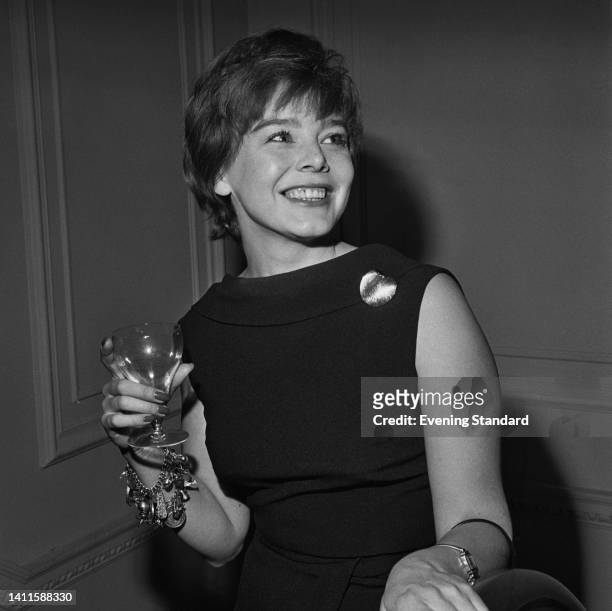 British actress Janet Munro wearing a sleeveless outfit, smiling with a drinking glass, attends an event, United Kingdom, 2nd April 1962.