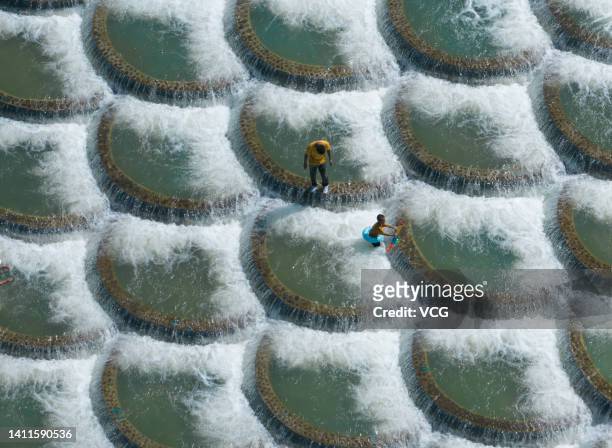 Tourists cool off at a location known for fish scale-shaped barriers that form small waterfalls during a hot summer day on July 28, 2022 in Xianfeng...
