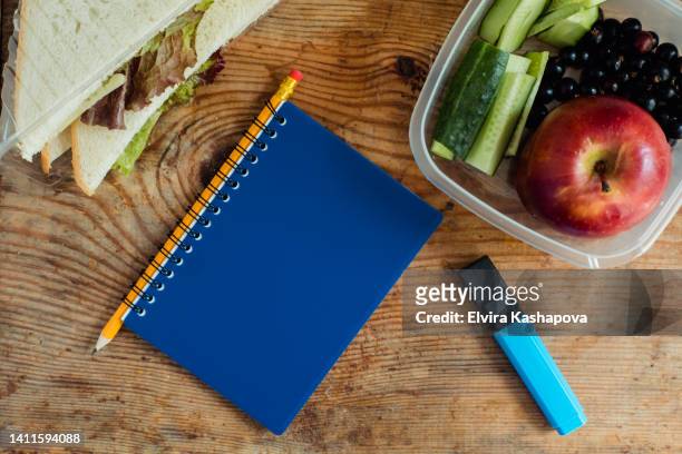 sandwich, blue notepad on rings with a simple pencil, with a blue marker and a lunch box with a red apple and cucumbers on a wooden background, top view - diet journal - fotografias e filmes do acervo