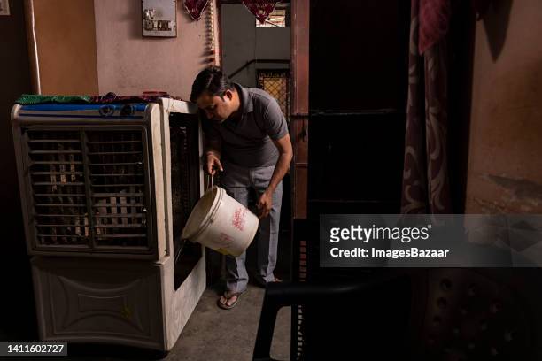 mid adult man filling air cooler with a bucket of water - air cooler stock pictures, royalty-free photos & images