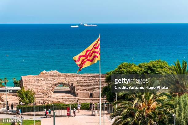 flag of tarragona waving. roman amphitheater and coast in the background. - ancient roman flag stock-fotos und bilder