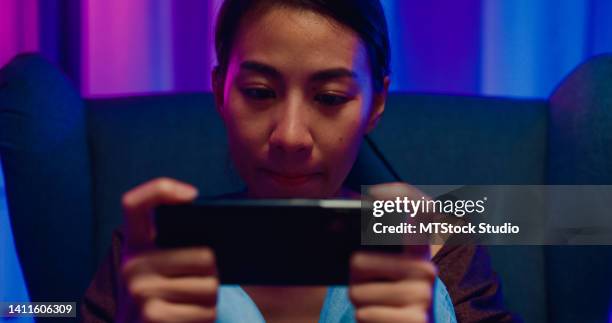 close-up aggressive young asian woman with shirt on sofa chair hold smartphone talk with friends feel upset angry for loser competition play online game in living room home at night. - glee tv program stockfoto's en -beelden