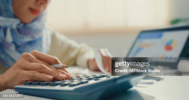 closeup asian muslim woman with hijab using tablet calculator focus on utility bills calculate check credit card receipt monthly expense bill in living room at house. - manage invest stock pictures, royalty-free photos & images