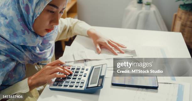 close up asian muslim woman with hijab using phone calculator focus on utility bills calculate check credit card receipt monthly expense bill in living room at house. - energy bill stock pictures, royalty-free photos & images