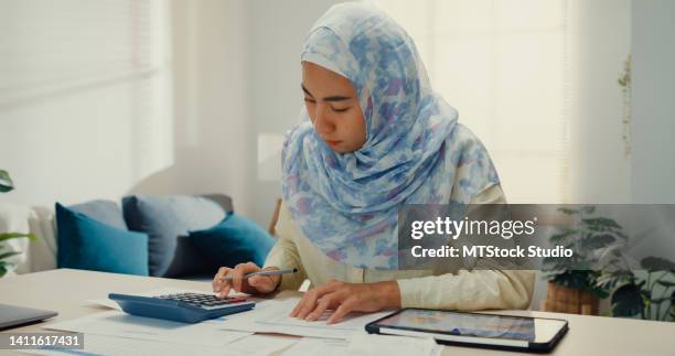 junge asiatische muslimische frau mit hijab mit tablet-rechner fokus auf stromrechnungen berechnen scheck kreditkartenbeleg monatliche spesenrechnung im wohnzimmer im haus. - steuerberater stock-fotos und bilder