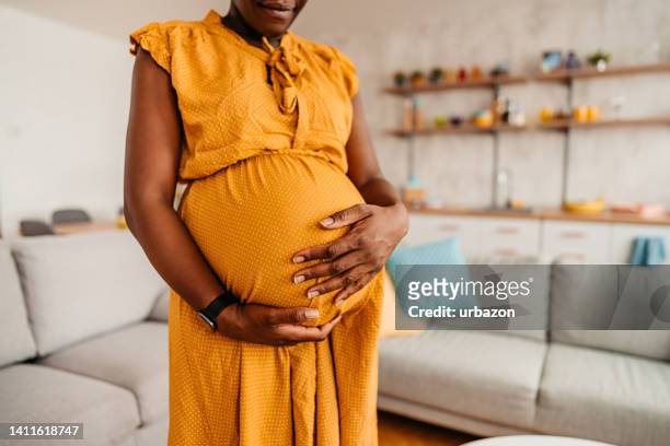 mujer negra disfrutando del embarazo en casa - embarazada fotos fotografías e imágenes de stock