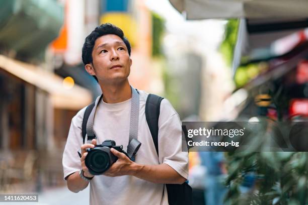 young male tourist taking photos with camera in streets of historical town during his travel - camera bag stockfoto's en -beelden