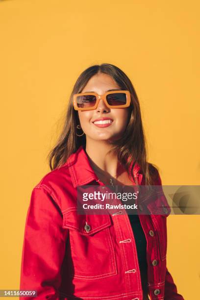 vertical photo of a young smiling girl with orange glasses on orange background - sunglasses woman stock pictures, royalty-free photos & images