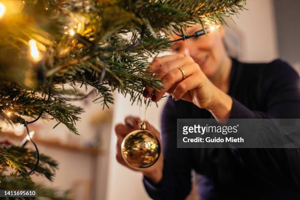 woman decorating christmas tree at home with golden christmas tree decorations. - weihnachtsbaum stock-fotos und bilder