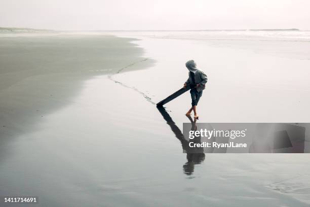 junge, der treibholz durch strandsand schleppt - boy exploring on beach stock-fotos und bilder