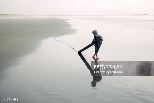 boy dragging driftwood through beach sand - boy exploring on beach stock pictures, royalty-free photos & images