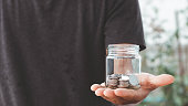Save money concept, man hand holding a glass jar piggy bank with coins money, saving money growth for future finance accounting. The concept of financial, banking, economizing and investment.