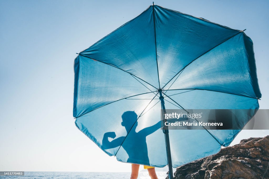 Silhouettes of boy flexing his muscles on blue beach umbrella.