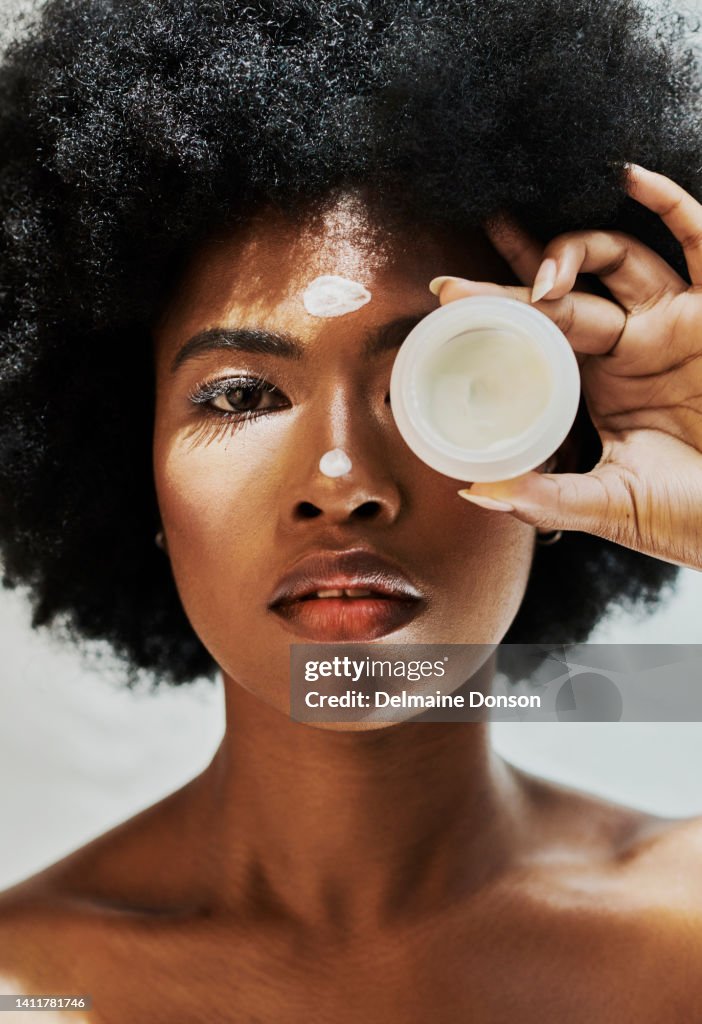 Afrikanisches weibliches Schönheitsmodell mit einer Afro-Werbelotion für die Hautpflege. Schöne schwarze Frau, die ihre Hautpflegeroutine macht und ihr Auge mit Serum bedeckt. Porträt einer Dame, die Creme aufträgt