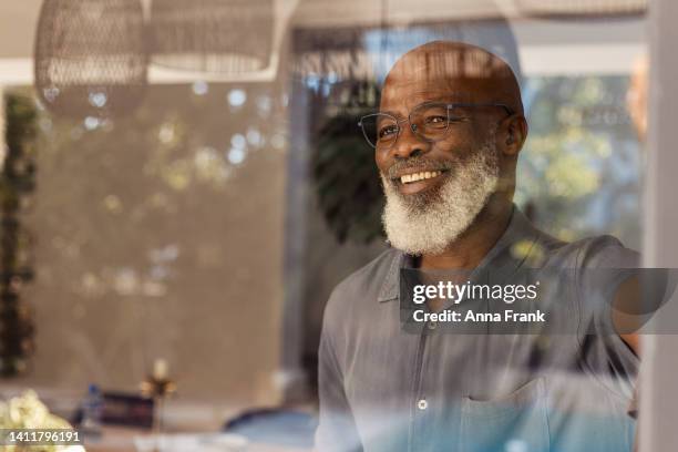 handsome senior man looking out through his window - black beard stock pictures, royalty-free photos & images