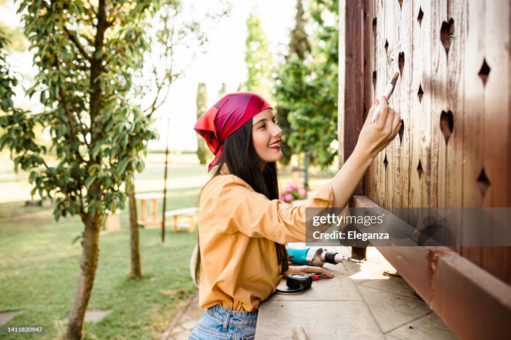 Young woman painting a wooden terrace