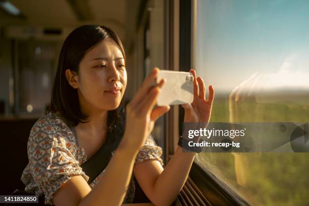 young female tourist taking photos through train window with her mobile phone - tåginteriör bildbanksfoton och bilder