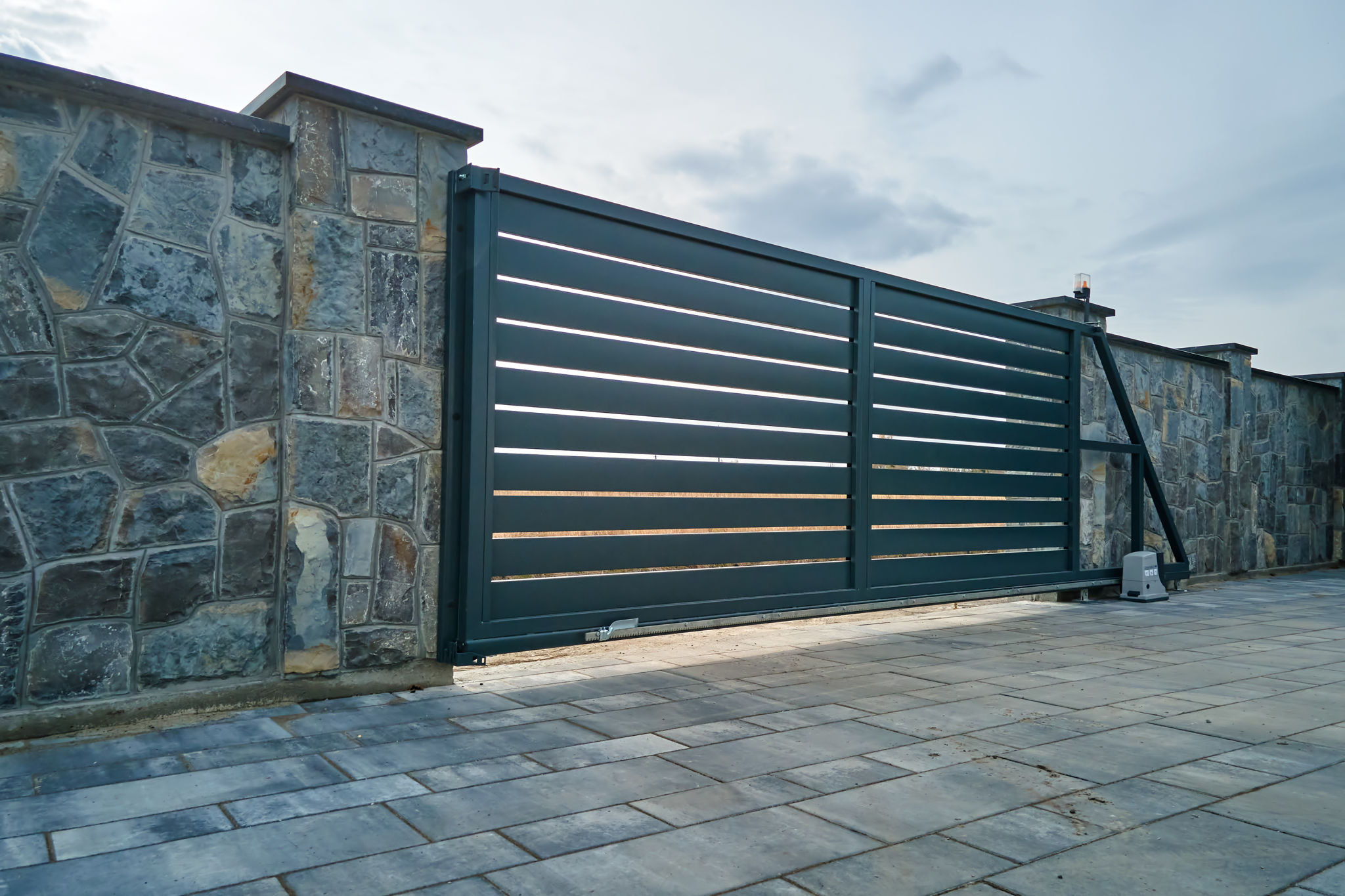 Wide automatic sliding gate with remote control installed in high stone fense wall. Security and protection concept Wide automatic sliding gate with remote control installed in high stone fense wall. Security and protection concept