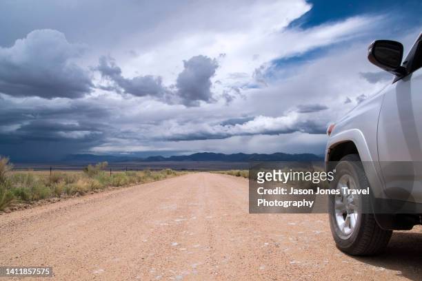 a car on a long straight gravel road with storm clouds on the horizon in colorado - suv berg stock-fotos und bilder