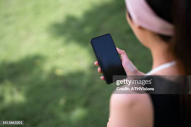 adult woman watching stock market on mobile phone while  having morning run exercise. over the shoulder view - terugkijken stockfoto's en -beelden