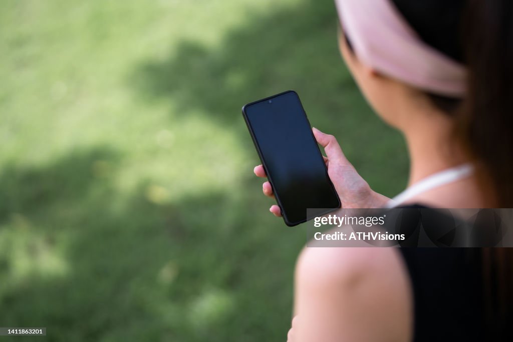 Adult woman watching stock market on mobile phone while having morning run exercise. Over the shoulder view