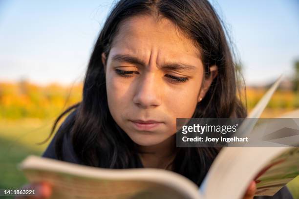 niña pre adolescente entrecierra los ojos para leer palabras en un libro - entrecerrar los ojos fotografías e imágenes de stock