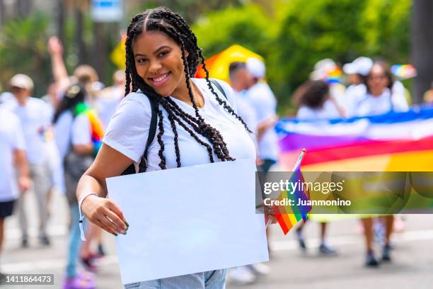 lächelnde junge frau, die einen weißen karton mit einem leeren schild in einer pride-parade hält - paradeplatz stock-fotos und bilder