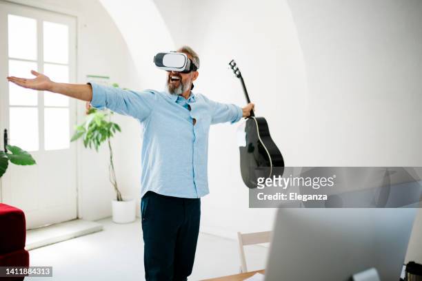 reifer mann, der in einer virtual-reality-brille im büro die akustische gitarre spielt - optical instrument stock-fotos und bilder