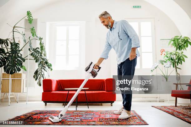uomo che pulisce la casa con l'aspirapolvere wireless - aspirapolvere foto e immagini stock