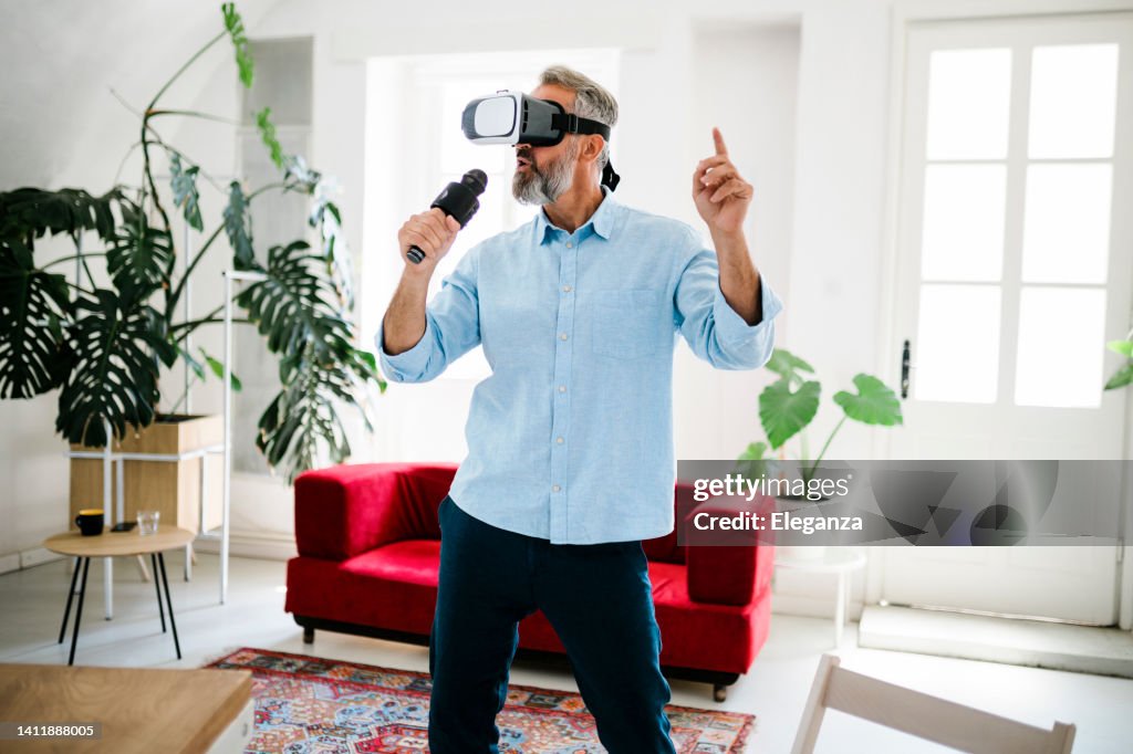 Mature man wearing glasses of virtual reality singing at karaoke while listening his favorite music at home