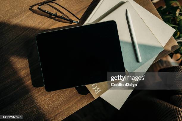 directly above shot of digital tablet, eyeglasses and books on rustic wooden table by houseplant against sunlight at home. digital tablet with blank screen for design mockup - book on table foto e immagini stock