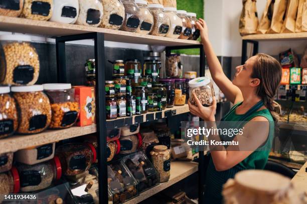 a saleswoman in an organic food store arranges jars of raw food on the shelf - gluten free stock pictures, royalty-free photos & images