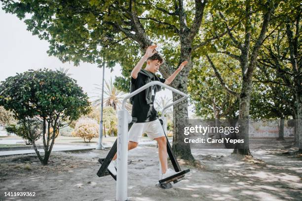 young male teenager doing some exercise in outdoor public gym - gymnastics equipment stock pictures, royalty-free photos & images