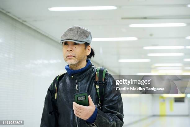 asian man walking alone on an urban underpass with a smartphone - underpass stock pictures, royalty-free photos & images