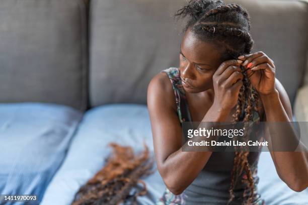 african woman making self african braids in her living room - alongamento de cabelo - fotografias e filmes do acervo