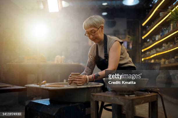 senior artist woman making clay bowl on pottery wheel. - cerámica fotografías e imágenes de stock