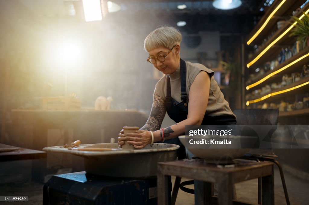 Senior artist woman making clay bowl on pottery wheel.
