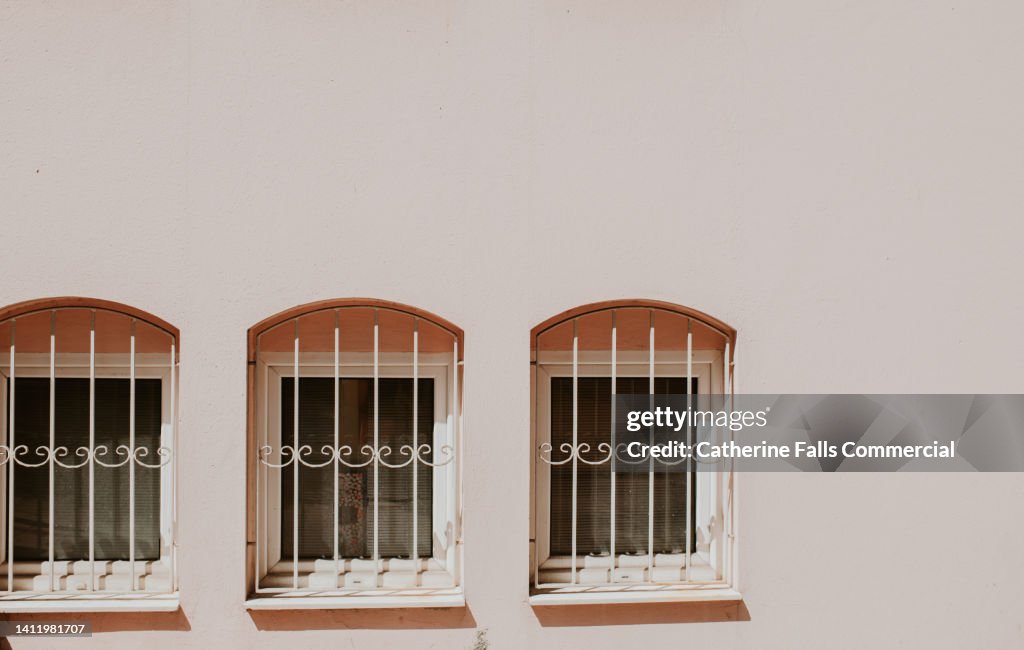 Three small windows set in a pink exterior wall with stylish bars