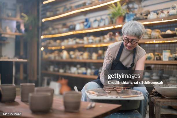 senior woman artist making clay bowl on pottery wheel in pottery studio. - senior hobbies stock pictures, royalty-free photos & images