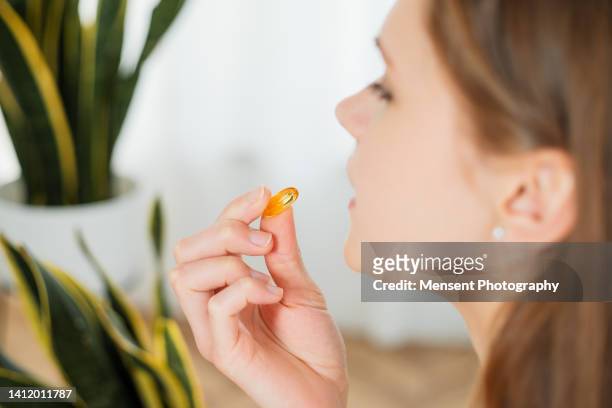 young woman ready taking pill omega-3 capsule in smiling close-up - vitaminas fotografías e imágenes de stock