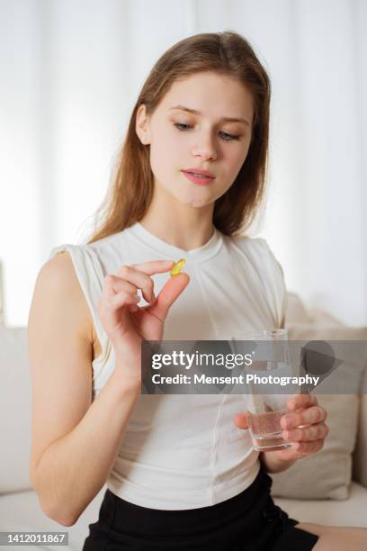 one young woman ready taking pill omega-3 vitamin and glass of water at home - huile de foie de morue photos et images de collection