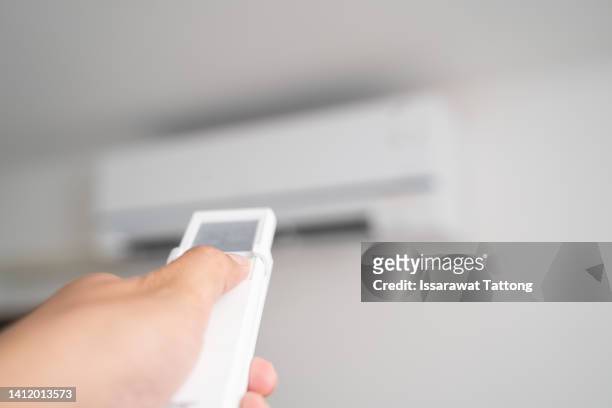 air conditioner inside the room with woman operating remote controller. / air conditioner with remote controller - air cooler stock pictures, royalty-free photos & images