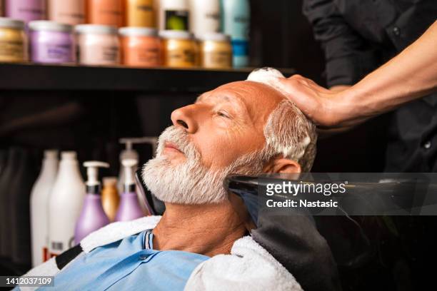 senior man sitting in chair washing his hair at hairdresser - hairdresser washing hair stock pictures, royalty-free photos & images